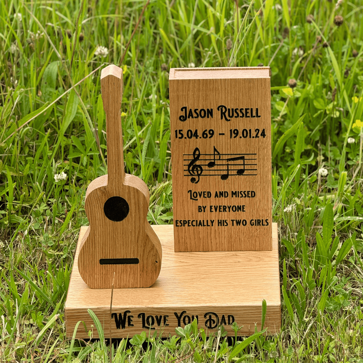 Wooden guitar-shaped ornament with engraved text on a grassy background