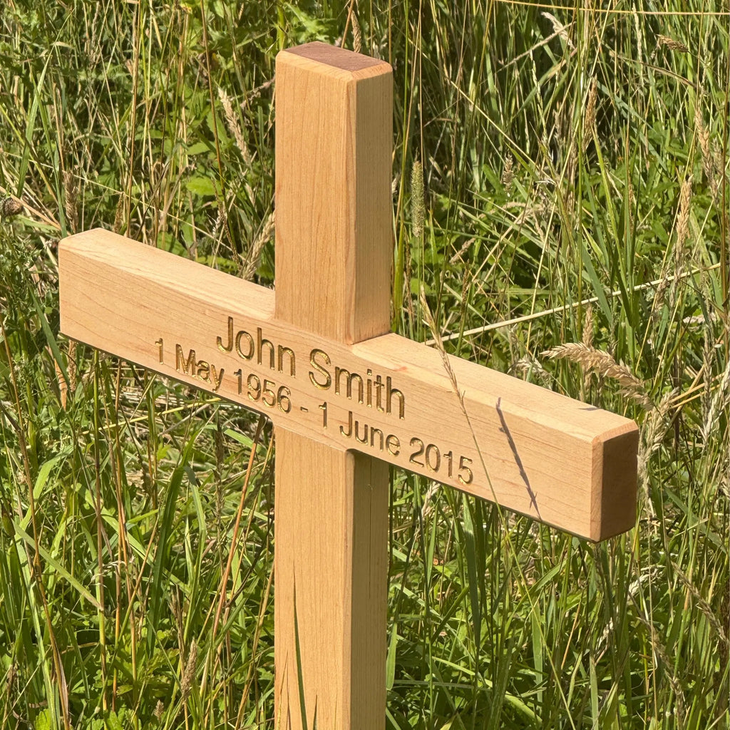 Wooden cross with engraved name and dates in a grassy field